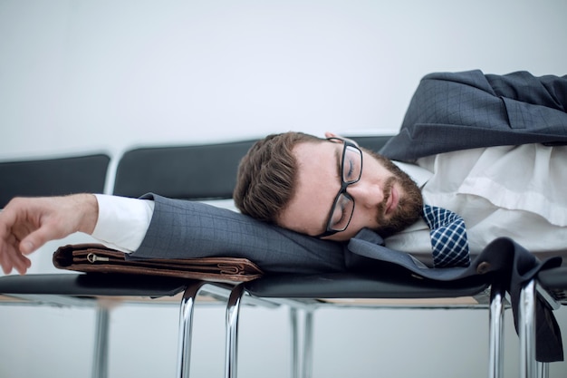 オフィスの廊下の椅子で寝ている疲れたビジネスマン