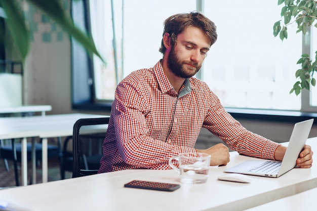 Tired businessman working on his computer in open space office