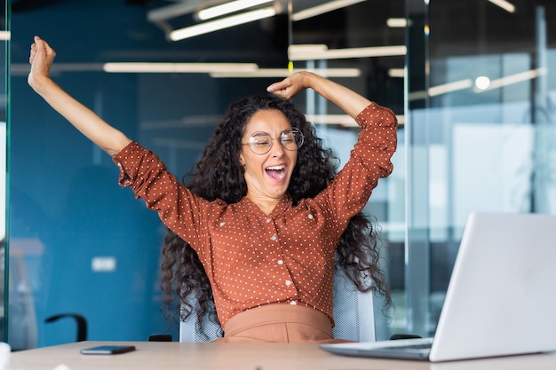 Tired businesswoman in office stretching and yawning latin american woman indoors working at