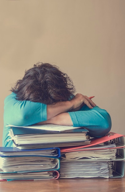 Photo tired businesswoman on stack of files at desk