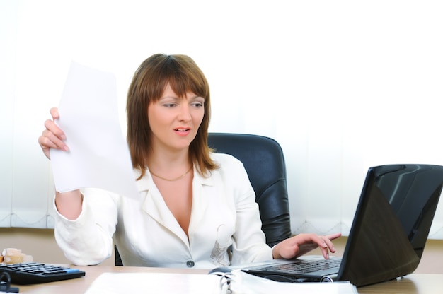 Tired caucasian white businesswoman uses paper sheet as fan and working at laptop in office