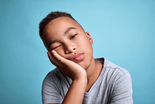 Tired child face on blue background depression while lazy thinking and rest on hand in studio Sad black boy with adhd bored kid with depressed insomnia and mental health fatigue in young children