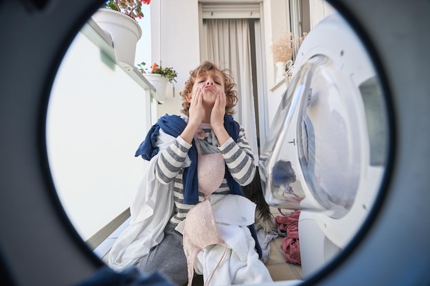 Tired child with laundry near washing machine