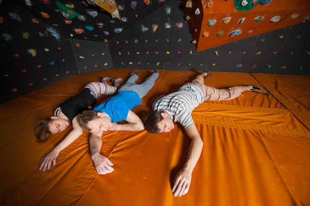 Tired climbers with closed eyes lying near rock wall indoors