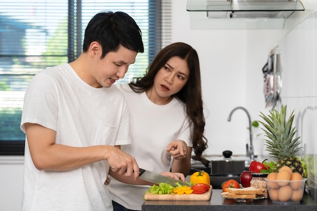 疲れたカップルが自宅のキッチンで野菜を調理して準備する怒っている女性が男性に手を指しています