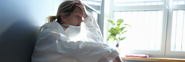 Tired doctor in protective antiplague suit sitting on corridor of clinic