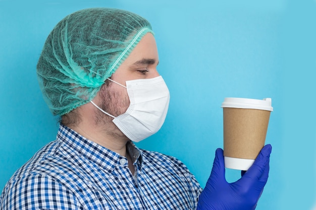 Tired doctor with coffee cup wearing coronavirus protective mask uniform.