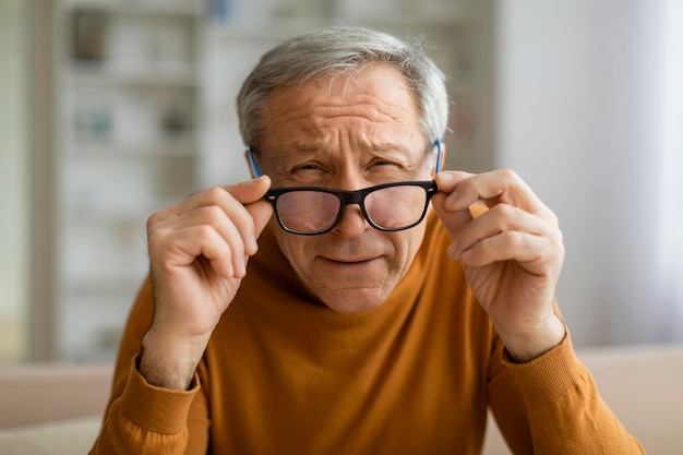 Tired elderly man removing eyeglasses home interior