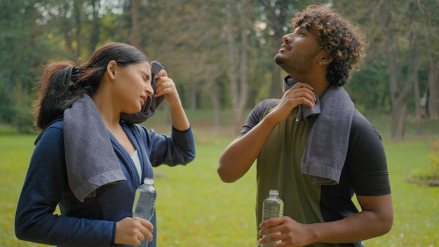 Tired exhausted indian man and woman relaxing after sports in park outdoor arabian fitness couple in