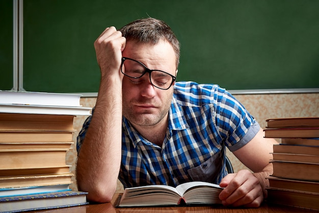 Studente stanco e sfinito dorme al tavolo con pile di libri.