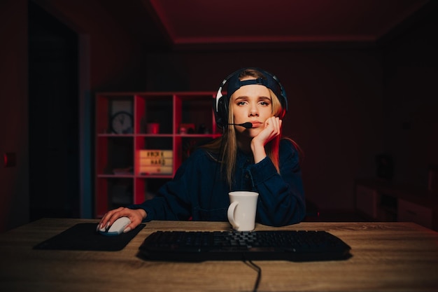 Tired female gamer in headset playing computer games at night\
at home staring intently at camera