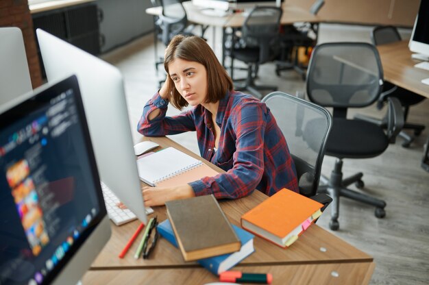 Tired female IT specialist works on computer in office. Web programmer or designer at workplace, creative occupation. Modern information technology, corporate team