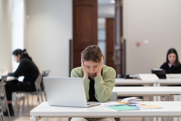 Tired female mature student sitting in library feeling unmotivated to study getting second degree