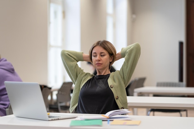 Photo tired female mature student taking break stretching arms while studying online in university library