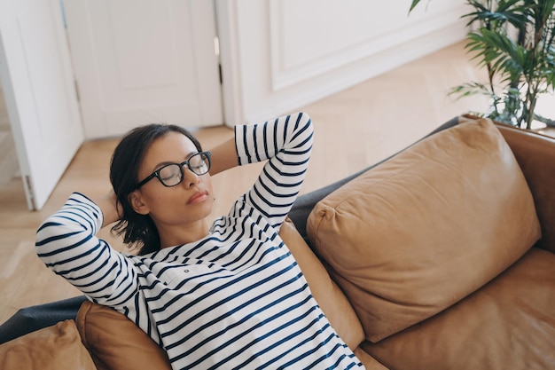 Tired female rests on sofa takes a break enjoys recreation sitting on comfortable couch at home