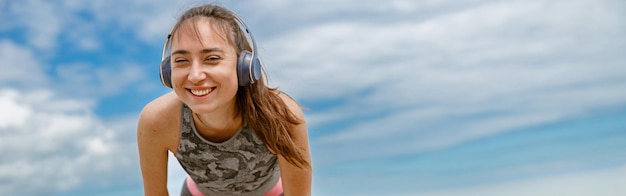 Tired female runner in headphones sweating after cardio exercise and rest after finish on beach