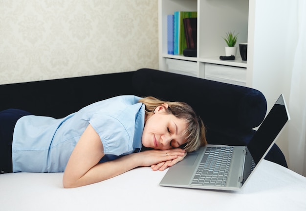 眠っている疲れた女性。ノートパソコンの前でリモートで作業する眠そうな少女