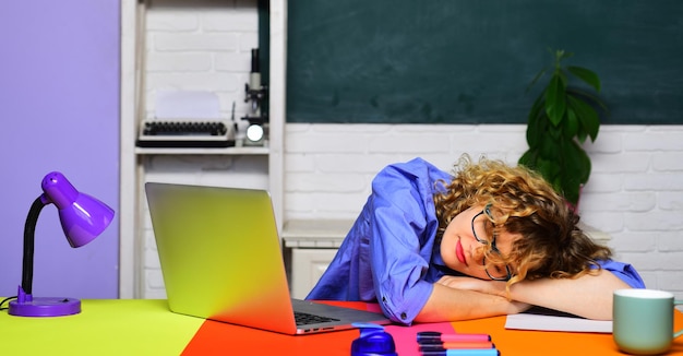 Tired female teacher in glasses sleeping at desk in classroom back to school knowledge day school