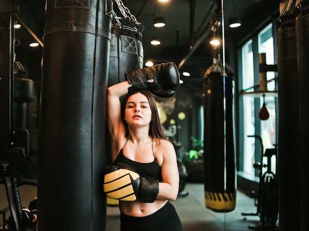 Tired fit woman resting after training near heavy bag at boxing room.