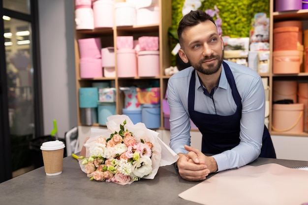 tired florist smiling looking at camera next to bouquet of flowers.