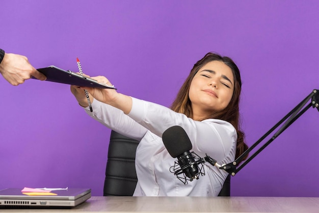 Tired girl doesn't want to take notebook Beautiful girl sitting behind the desk on purple background High quality photo