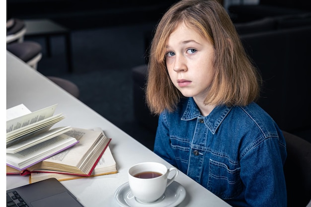 A tired girl in front of a laptop with a cup of tea and books