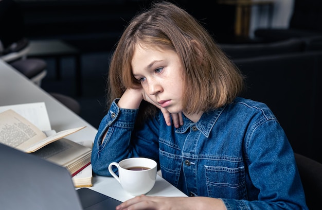 Tired girl in front of a laptop with a cup of tea and books