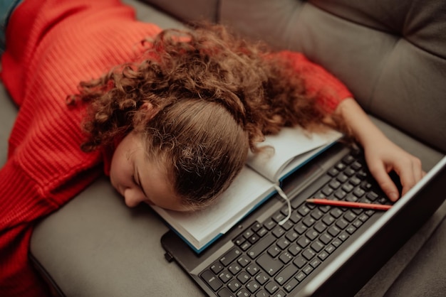 Tired girl is sleeping next to a laptopTired girl from distance learning at homeOnline education for kids during quarantine