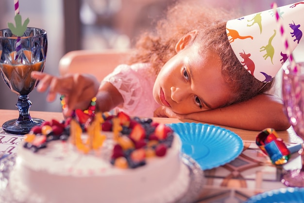 Ragazza stanca seduta al tavolo e guardando la sua torta di compleanno