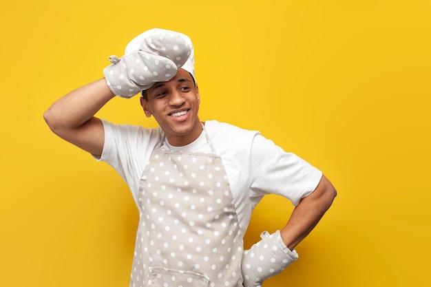 tired guy african american baker in an apron and gloves looks at copy space on yellow background