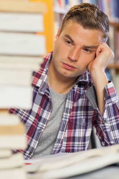 Foto studente bello stanco che studia fra le pile di libri