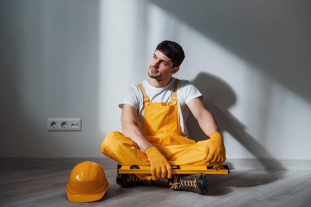 Photo tired handyman in yellow uniform sits indoors and takes break house renovation conception