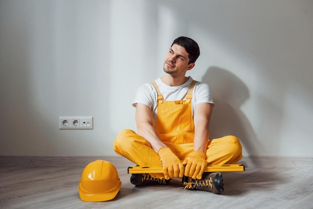 Tired handyman in yellow uniform sits indoors and takes break House renovation conception