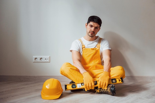Усталый разнорабочий в желтой форме сидит в помещении и делает перерыв Концепция ремонта дома