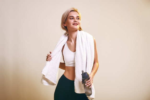 Tired but happy cute and young sporty woman in sports clothing with towel on shoulders