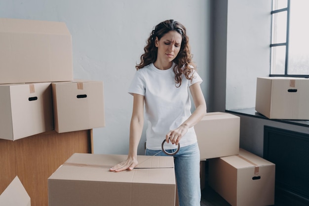 Tired hispanic woman packs parcels boxes using duct tape frowning Overtime delivery service