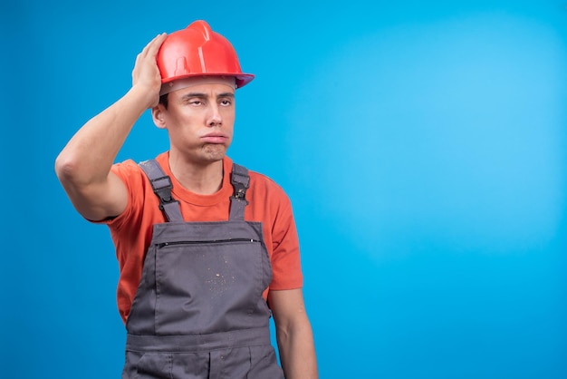 Tired male builder in uniform touching hardhat
