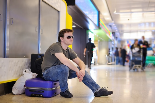 Passeggero maschio stanco all'aeroporto che si siede sulle valigie