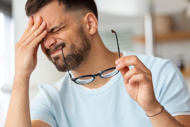 疲れた男性がメガネを外してマッサージする目は、強い頭痛に苦しむ疲労感を感じ、疲れ果てた体調不良の男性は、仕事に圧倒され、眼精疲労や乱視を持っています。健康問題の概念