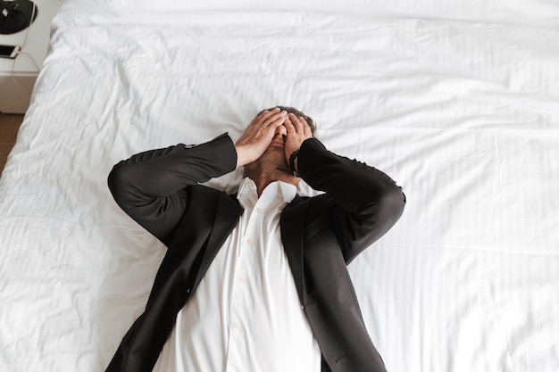 Tired man dressed in suit lying on bed