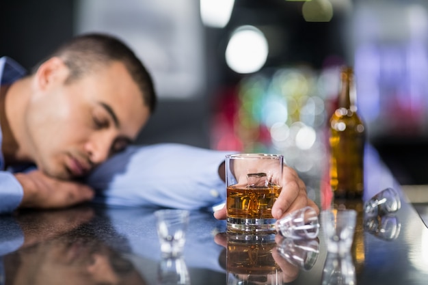 Foto uomo stanco che mangia un whisky e che dorme su un contatore