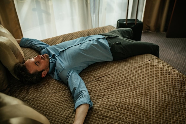 Tired man lying on the bed in a hotel room