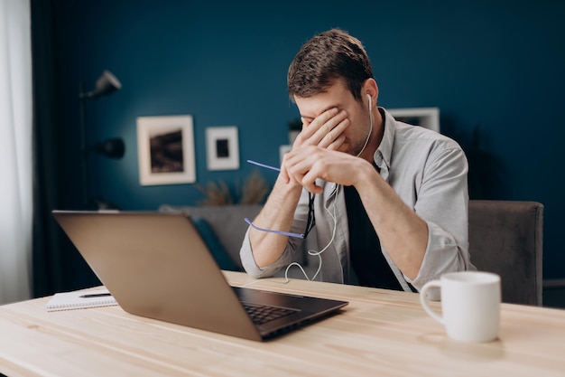 Tired man rubbing eyes after long working day with laptop