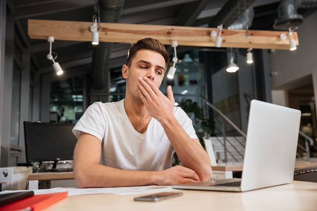 Tired man sitting by the table and coning his mouth in office.