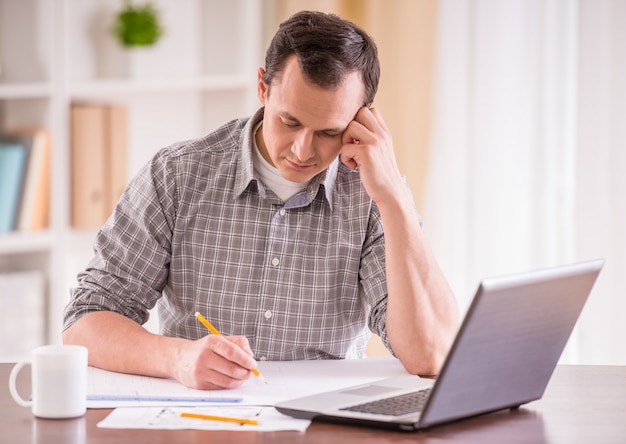 Tired man sitting at table with laptop and working.