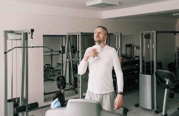 A tired man wipes sweat from his face with a towel after working out on a treadmill. cardio workout