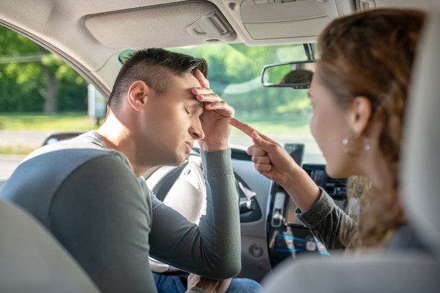 Tired man with closed eyes driving car and next to woman