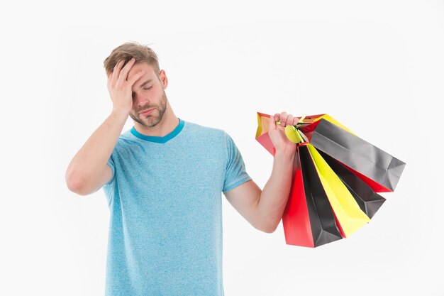 Tired man with shopping bags isolated on white. Macho with colorful paper bags. Fashion shopper in casual blue tshirt and shorts. Holidays preparation and celebration. Shopping sale on black friday.