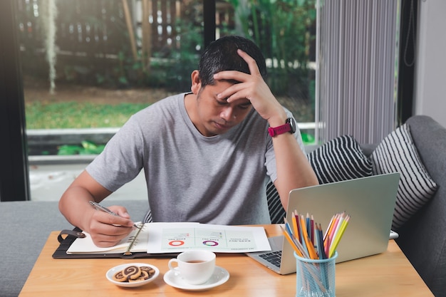 Uomo stanco che lavora a casa con matite, caffè e snack