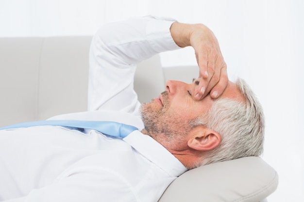 Tired mature businessman resting on sofa in living room